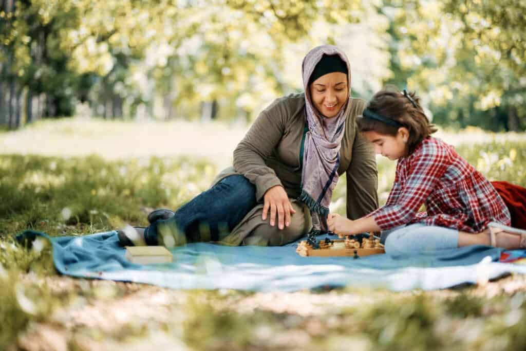 Happy Muslim mother playing chess with her daughter in the park.